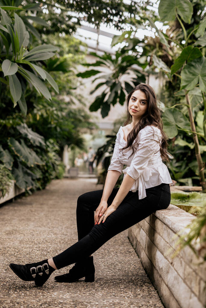 Belle femme attrayante assise en chemisier blanc et pantalon noir regarder à la caméra. Jeune femme avec fond de nature - Photo, image