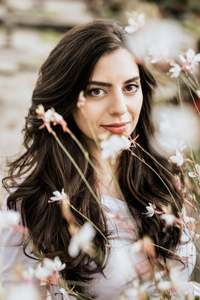 Vertical photo of beautiful young woman surrounded by flowers outdoor. Brunette woman on fresh flower background - Φωτογραφία, εικόνα