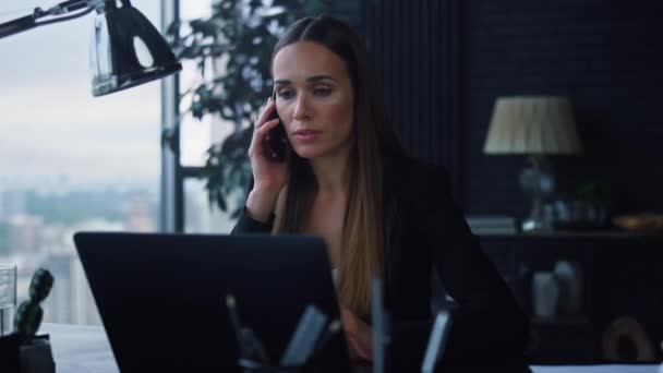 Geschäftsfrau, die im Büro mit dem Smartphone spricht. Frau blickt auf Laptop-Bildschirm - Filmmaterial, Video