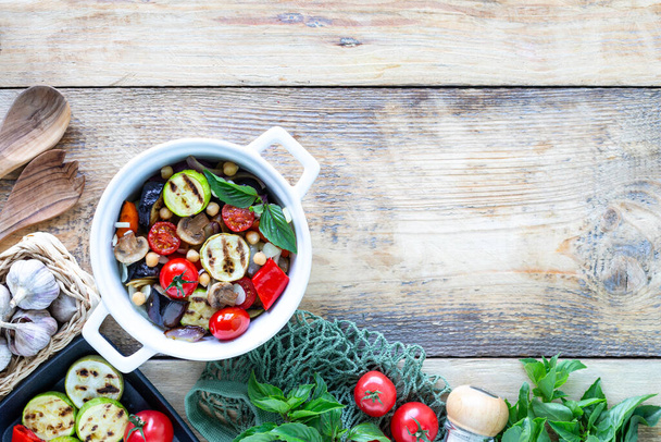 Gegrilltes Gemüse in einer weißen Keramikpfanne mit Zutaten auf rustikalem Hintergrund. Vegetarisches Essen. Ansicht von oben. - Foto, Bild