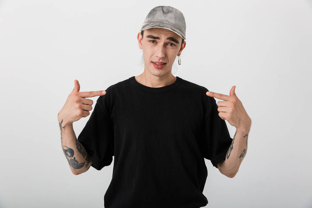 Portrait closeup of handsome confused man wearing black clothes looking at camera and pointing fingers at himself over white background - Foto, Imagen
