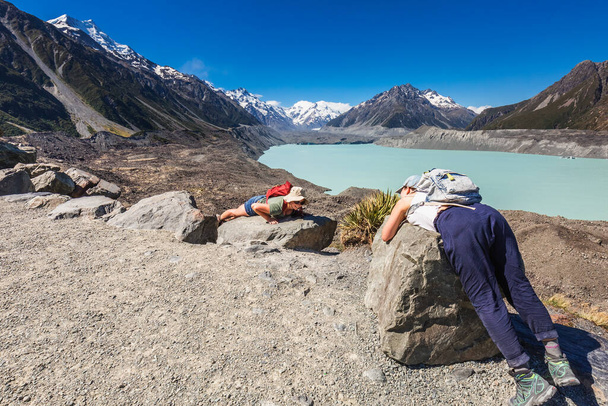 Жіночі туристи відпочивають на скелях на животі в льодовиковому озері. Льодовик Тасман, Аоракі - Маунт-Кук, Нова Зеландія. Гора Кук, Нова Зеландія - 24 грудня 2017. - Фото, зображення