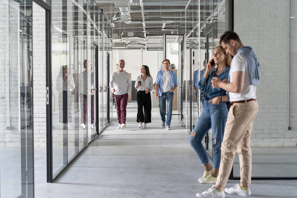 Полная длина молодых современных людей в элегантной повседневной одежде, имеющих обсуждение во время прогулки по офису - Фото, изображение