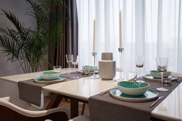 Familie evenement concept. Hedendaags interieurontwerp in keuken in modern huis met bord, bestek, glaswerk en decor op tafel op eetplaats - Foto, afbeelding