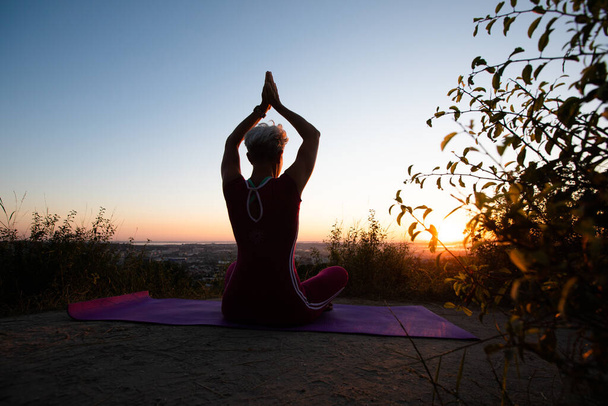 Black foto Woman back view holding hands up while sitting in lotus position on morning sunrise - Photo, Image
