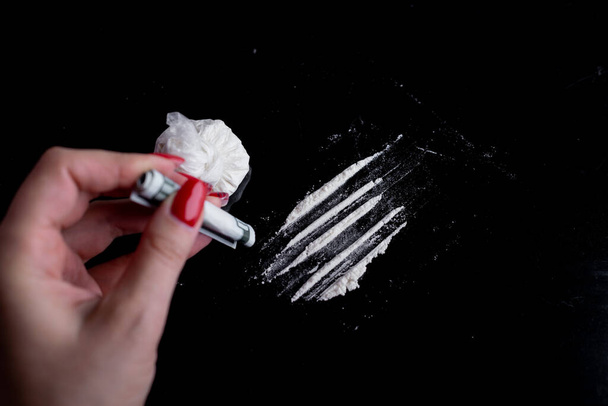 poudre blanche (héroïne, cocaïne, narcotique) dans un sac plastique sur fond noir, les drogues sont dispersées sous la forme d'un chemin, une main avec un bec plié dans un tube - Photo, image