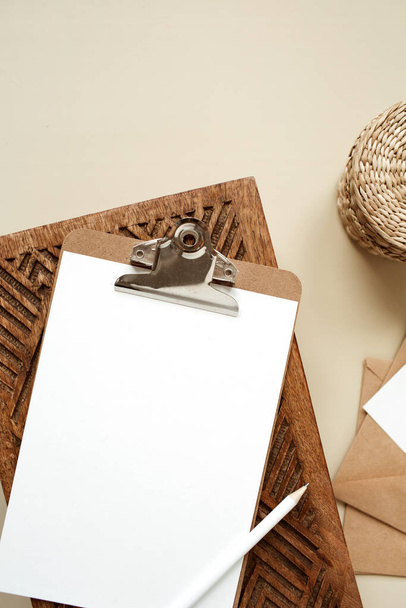 Clipboard tablet pad with blank paper sheet on beige table. Artist home office desk workspace with wooden casket, pencil, envelopes and stationery. Flat lay, top view mockup with empty copy space - Foto, Imagen