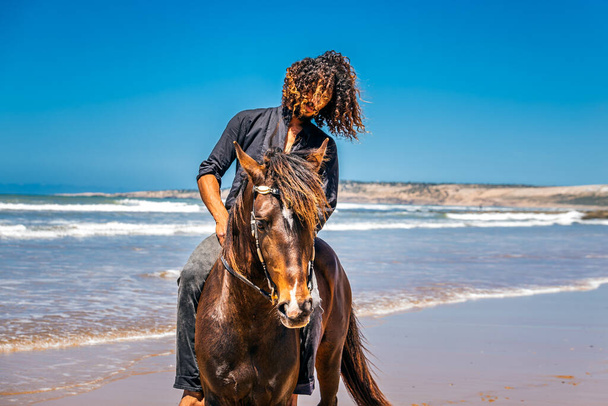 Hezký muž s dlouhými vlasy jezdí na koni na pláži. Essaouira, Maroko - 14. dubna 2016. - Fotografie, Obrázek