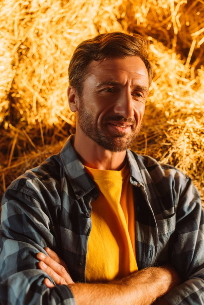 farmer kockás ingben a szénabála mellett, a napsütésben félrenéz. - Fotó, kép
