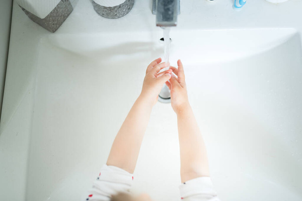 Симпатичная девочка 2-3 лет мыла руки с мылом и водой в светлой ванной комнате. Вид сверху - Фото, изображение
