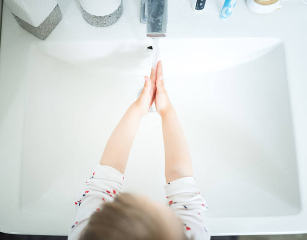 Petite fille mignonne de 2-3 ans se lavant les mains avec du savon et de l'eau dans une salle de bain lumineuse. Vue du dessus - Photo, image