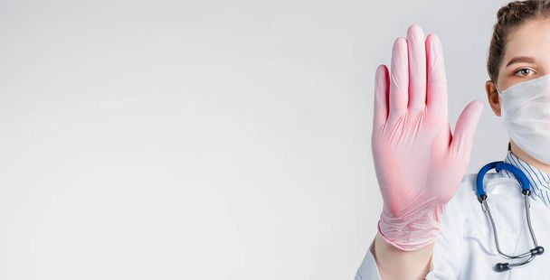 Młoda piękna lekarka w białym płaszczu i różowych jałowych rękawiczkach pokazuje gest zatrzymania na białym tle. Powiedz, żadnych chorób wirusowych. Skopiuj miejsce na tekst - Zdjęcie, obraz