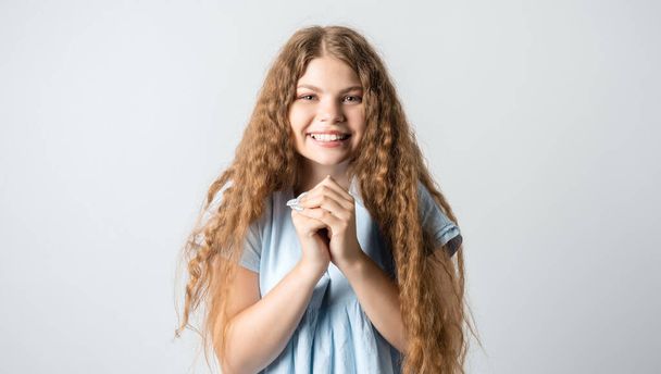 Фотографія харизматичної європейської молодої жінки з кучерявим довгим волоссям тримається разом поруч підборіддя, ніжно посміхається, має милий вираз, носить синю футболку.. - Фото, зображення