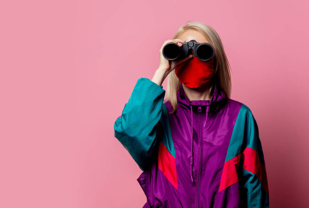 Woman in face mask and 80s clothes with binoculars on pink background - Photo, Image