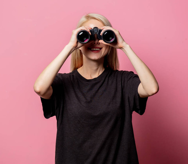 Woman in black t-shirt with binoculars on pink background  - Photo, Image