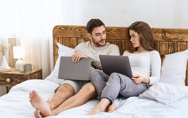現代の夜のレジャー。男と女はノートパソコンとベッドの上に横になって話す - 写真・画像
