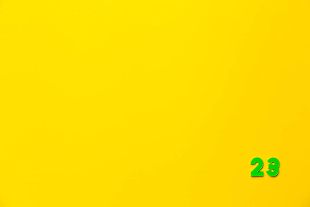 Um brinquedo de plástico verde número vinte e três está localizado no canto inferior direito em um fundo amarelo. - Foto, Imagem