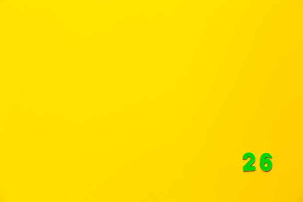 Um brinquedo de plástico verde número vinte e seis está localizado no canto inferior direito em um fundo amarelo. - Foto, Imagem
