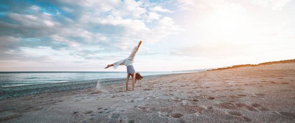 Young girl is doing yoga on the beach at sunset - Foto, Imagen