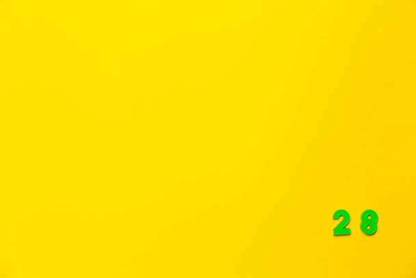 Um brinquedo de plástico verde número vinte e oito está localizado no canto inferior direito em um fundo amarelo. - Foto, Imagem