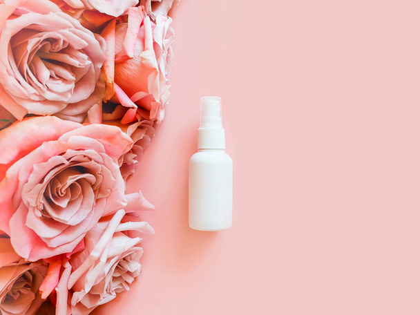 Mockup από μη επώνυμα λευκό πλαστικό μπουκάλι σπρέι και ροζ τριαντάφυλλα σε παστέλ ροζ φόντο. Μπουκάλι για μαρκάρισμα και ετικέτα. Φυσικά οργανικά καλλυντικά spa και υγρό αντιμικροβιακό σπρέι. Άνω όψη - Φωτογραφία, εικόνα