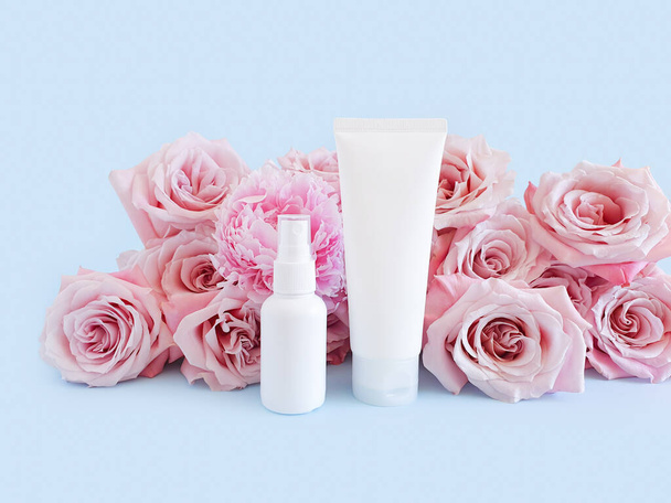 Két márkátlan fehér palack makettjei a márkázáshoz és címkézéshez, valamint világos rózsaszín rózsák pasztell kék háttérrel. Az egyik a műanyag csövek összenyomása. Egyéb műanyag spray palack. - Fotó, kép