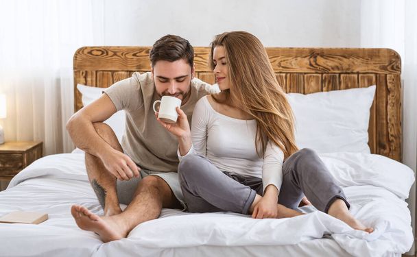 Romantische koffie in bed. glimlachende vrouw geeft haar man drinken uit beker in interieur - Foto, afbeelding