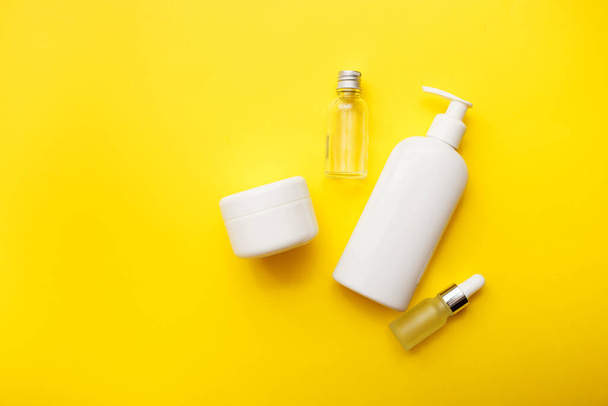 Cosmetics bottles on bright yellow background, top view, copy space. Mock up. White jars, bath accessories. Face and body care concept. - Photo, Image
