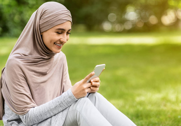 Cheerful muslim girl chatting with friends on mobile phone - Photo, Image