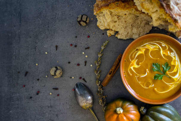 Pumpkin soup with fresh baked bread and silver spoon on gray table. Top view photo of vegan meal. Healthy eating concept. Dark textured background with copy space.  - 写真・画像