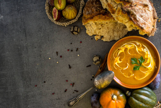 Pumpkin soup with fresh baked bread and silver spoon on gray table. Top view photo of vegan meal. Healthy eating concept. Dark textured background with copy space.  - 写真・画像