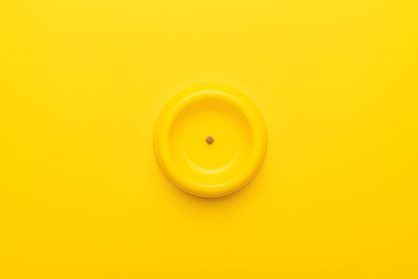 Yellow pet bowl with dry food leftovers over yellow background - Fotó, kép