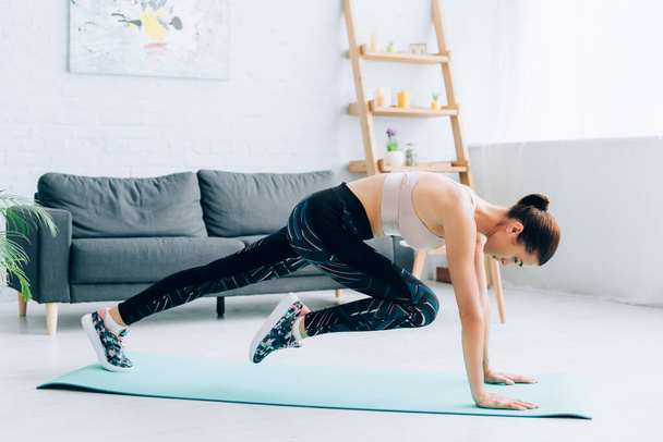Side vie of fit sportswoman exercising in living room  - Foto, Bild