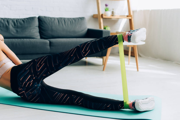 Cropped view of sportswoman working out with resistance band in living room  - Zdjęcie, obraz