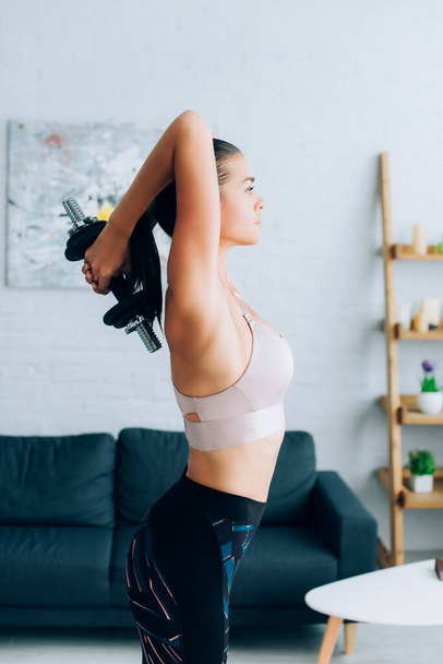 Side view of fit sportswoman exercising with dumbbell at home  - Foto, Imagem