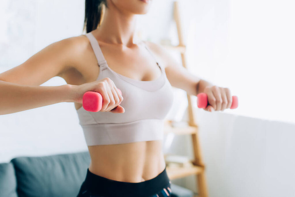 Cropped view of sportswoman exercising with pink dumbbells at home  - Photo, Image