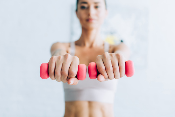 Selective focus of sportswoman training with dumbbells at home  - Foto, imagen