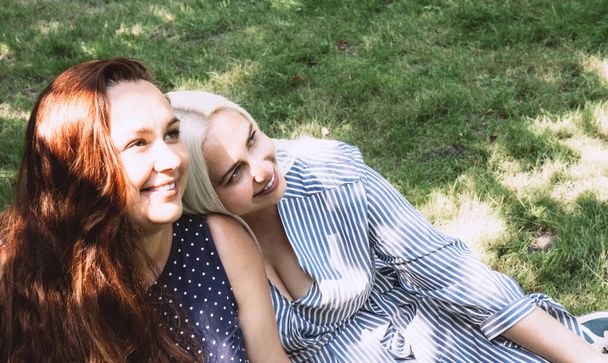 Zwei schöne junge Frauen sitzen nebeneinander im Gras. Reden wir. Glückliches Paar junger lesbischer Frauen. Nahaufnahme. Seitenansicht - Foto, Bild