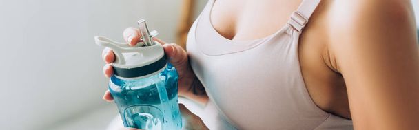 Panoramic crop of sportswoman holding sports bottle at home  - Photo, Image