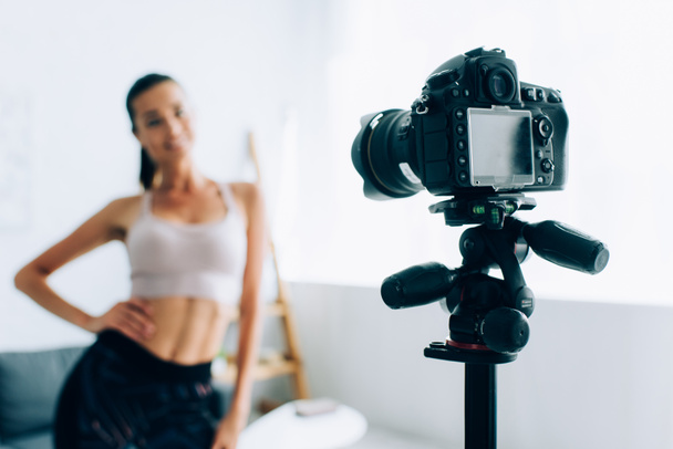 リビングルームのフィットスポーツ女性の横に三脚にデジタルカメラの選択的な焦点  - 写真・画像