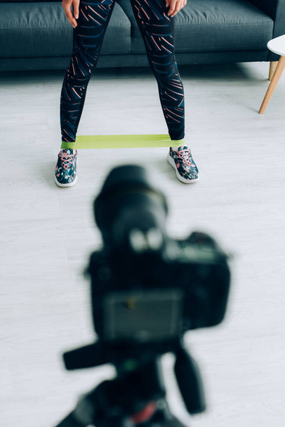 Selektywne skupienie sportowca z pasem oporu na nogach stojących w pobliżu aparatu cyfrowego w domu  - Zdjęcie, obraz