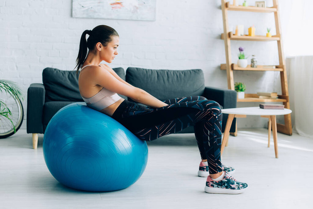 Side view of sportswoman working out on fitness ball in living room  - Foto, afbeelding