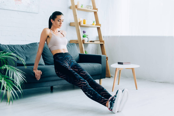 Selective focus of sportswoman exercising near couch in living room  - Foto, afbeelding