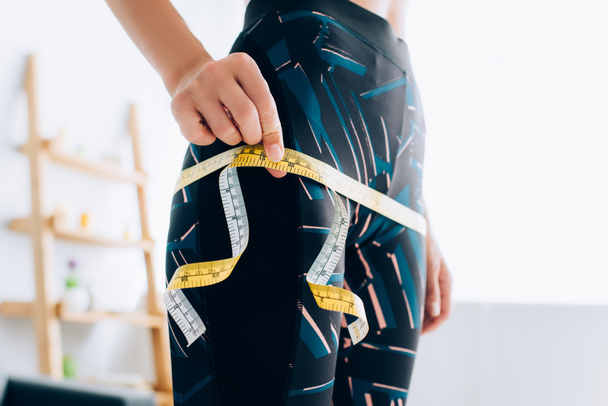 Cropped view of sportswoman measuring hips with tape - Zdjęcie, obraz