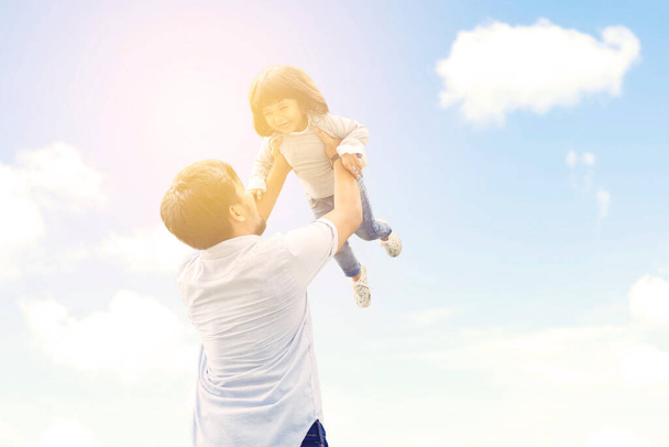 Happy young father playing and lifting his daughter under clear sky during sunny day - Foto, imagen