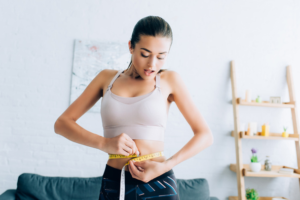 Excited sportswoman measuring waist with tape at home  - Photo, Image