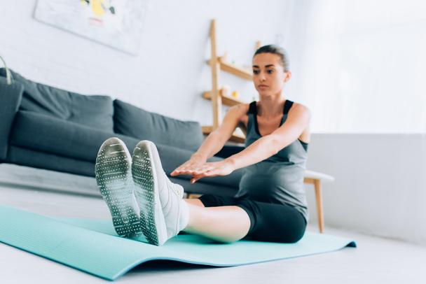Selective focus of pregnant woman stretching while exercising on fitness mat at home  - Fotografie, Obrázek