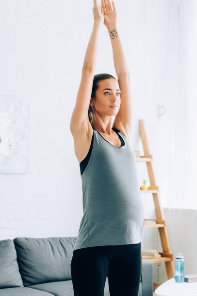 Pregnant sportswoman looking away while exercising at home  - Foto, immagini