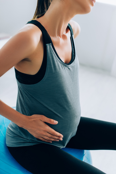 Vista recortada de la mujer embarazada en ropa deportiva sentado en la pelota de fitness  - Foto, imagen