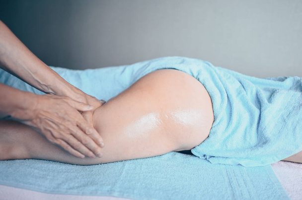 Νεαρή αγνώριστη γυναίκα ξαπλωμένη στο τραπέζι του μασάζ και απολαμβάνοντας το θεραπευτικό μασάζ. Φροντίδα σώματος, απώλεια βάρους. Θεραπευτής μασάζ χεριών μασέρ κάνοντας μασάζ κατά της κυτταρίτιδας σε κλινική σπα - Φωτογραφία, εικόνα